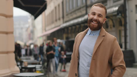 caucasian good looking businessman in a coat turning to the camera and smiling joyfully in the street in autumn