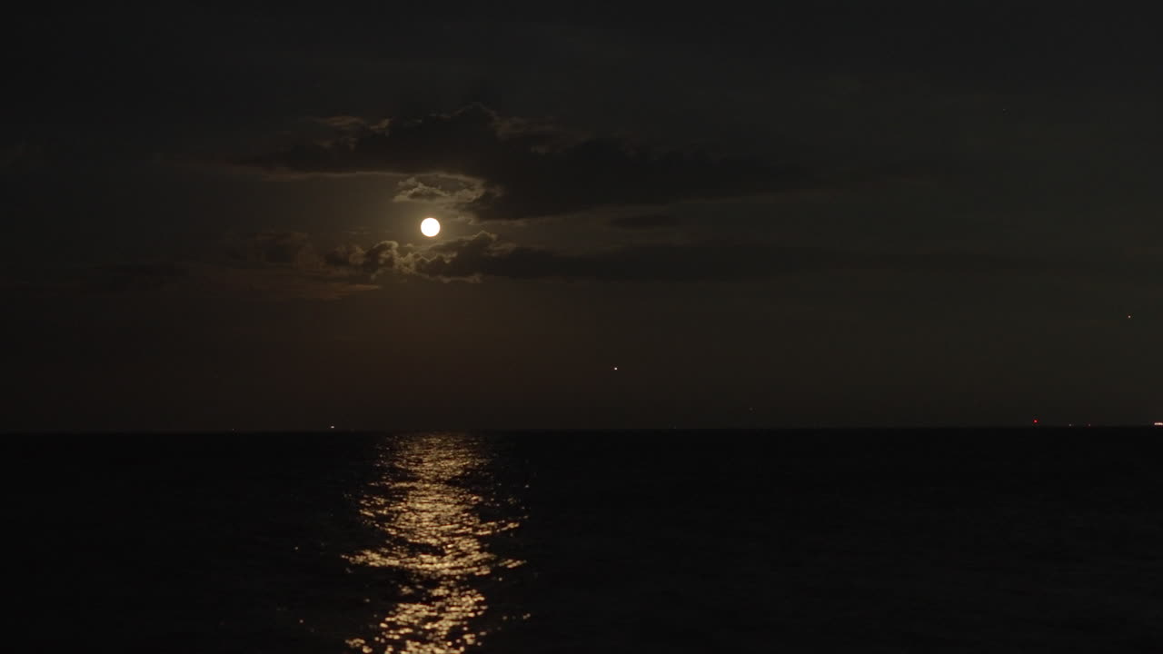 A majestic Strawberry Solstice Moon ascends over Lake Michigan from a Chicago lakefront. 4K time-lapse captures vibrant celestial hues, soft moonlight, and calm water reflections in a tranquil scene.