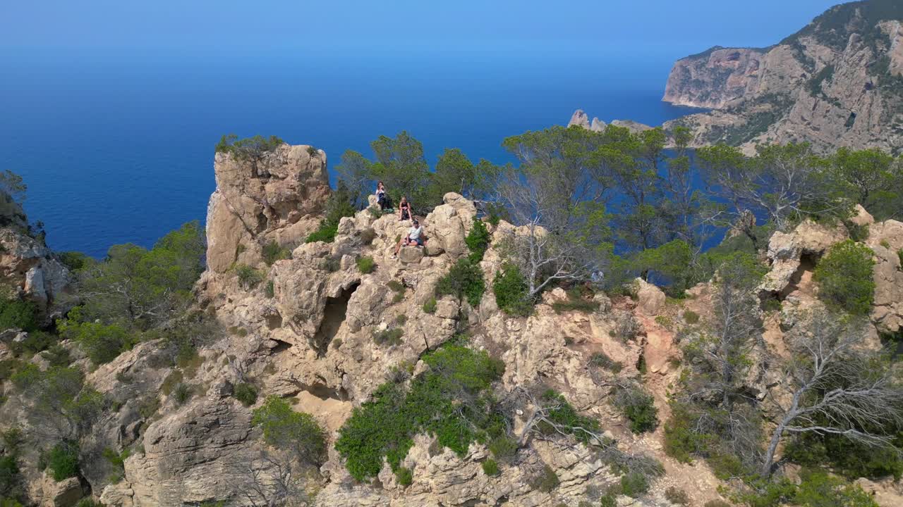 Gruppo di turisti che fanno trekking su una scogliera rocciosa a Ibiza, Spagna, godendosi la vista mozzafiato del Mar Mediterraneo. Bella ripresa aerea con drone in ascesa