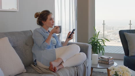 Hermosa-Joven-Usando-Un-Teléfono-Inteligente-Relajándose-En-El-Sofá-En-Casa-Navegando-Mensajes-De-Texto-En-Línea-Tomando-Café-Disfrutando-De-Un-Estilo-De-Vida-Cómodo