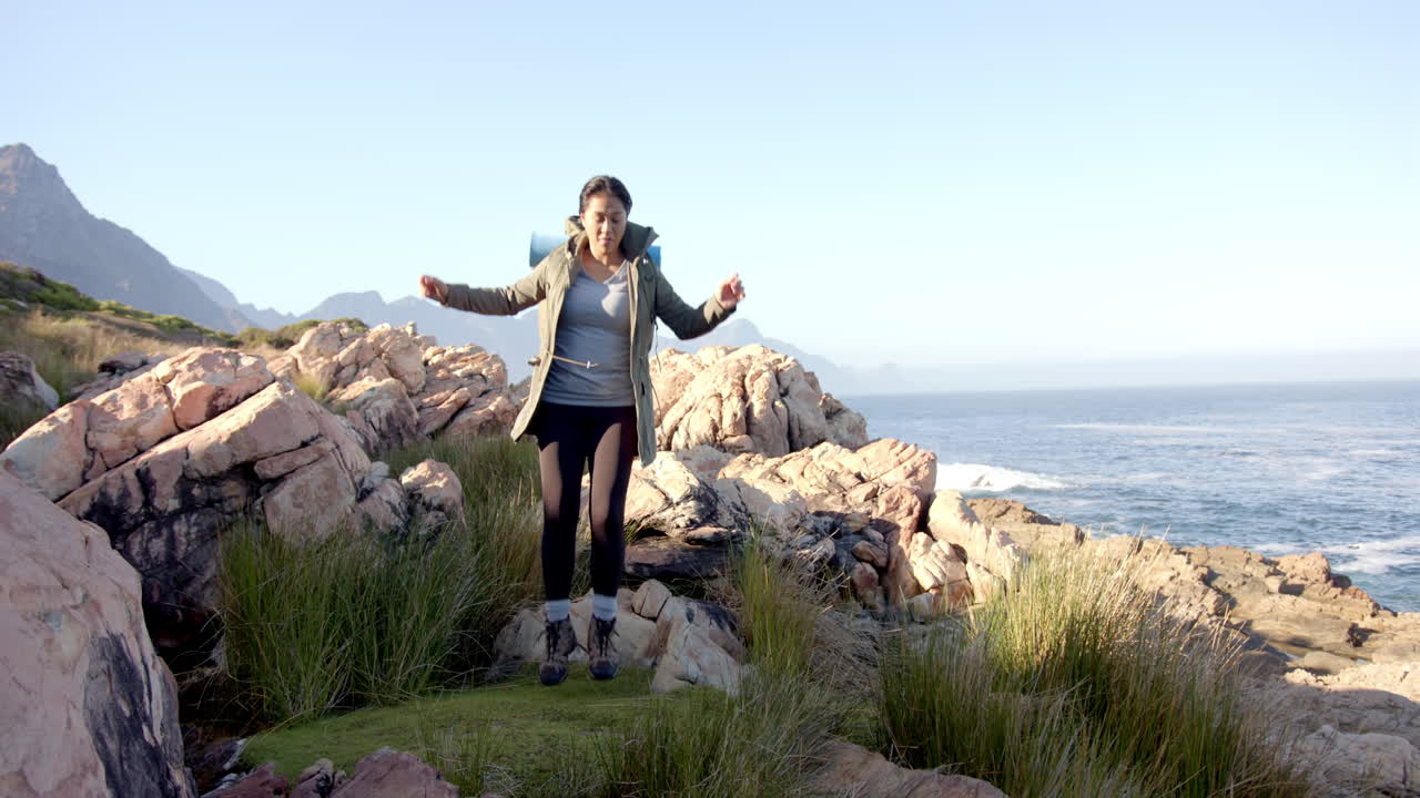 Hiking in mountains, woman standing on rocky terrain near ocean, smiling