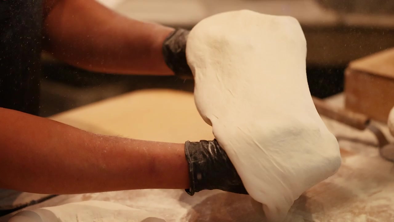 Close-up of a chef's hands spinning and stretching pizza dough in a professional kitchen.