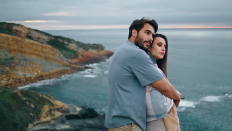 casal pacífico de pé na colina da costa olhando para a paisagem marinha sombria. homem abraçando mulher