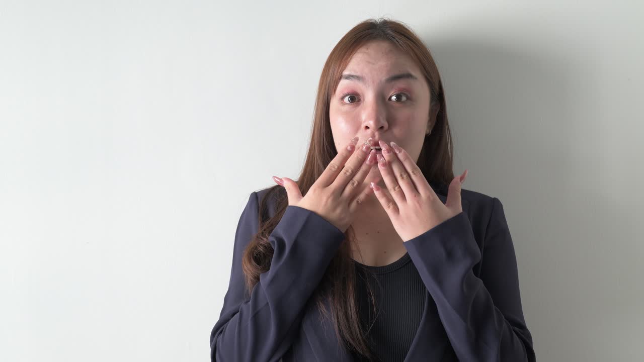 白い背景を背に、衝撃を受け驚いている若いアジア人女性ビジネスパーソンのポートレート。