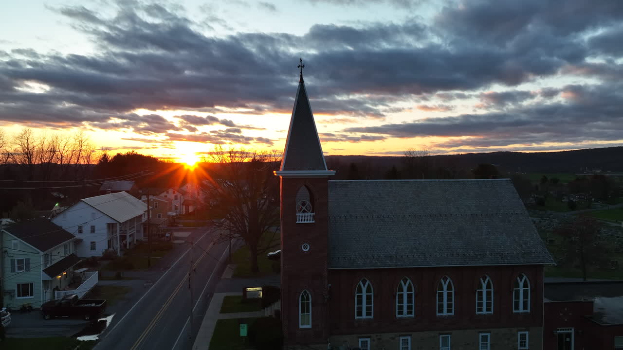 Church in rural community in USA at sunset. Truck with headlights on drive by at night. Winter sunset aerial.
