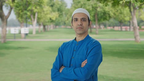 portrait of confident muslim man standing crossed hands in park