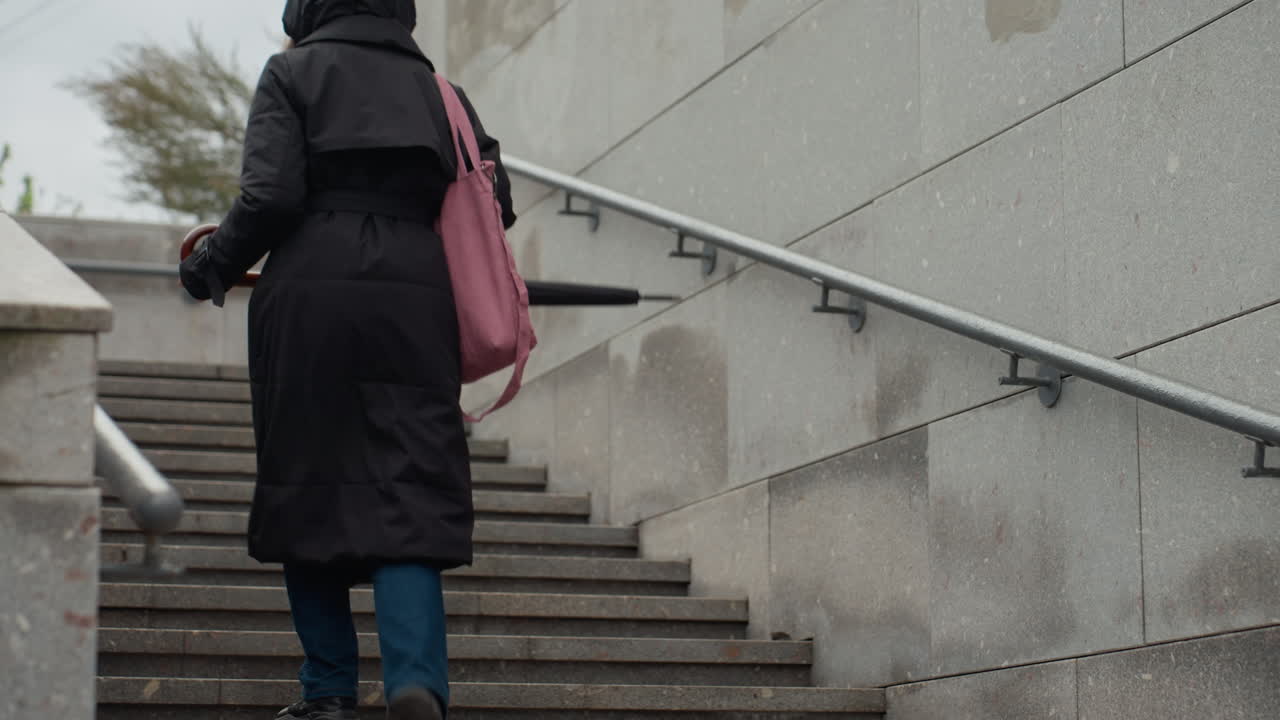 Bybo går op ad betontrapper. Kvindelig fodgænger med pink taske går målrettet op i byen. Kvinde klædt afslappet med pink taske bestiger selvsikkert en trappe midt i byen uanset vejret