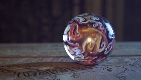 esfera de vidrio colorida girando lentamente en la tela ornamentada del tarot, revelando movimientos sutiles dentro del ambiente místico y sombrío de la adivinación y la exploración espiritual