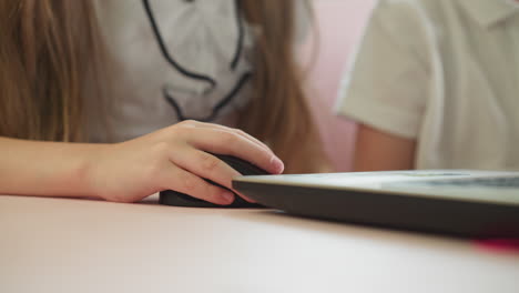 Little-girl-moves-mouse-using-laptop-with-brother-at-table