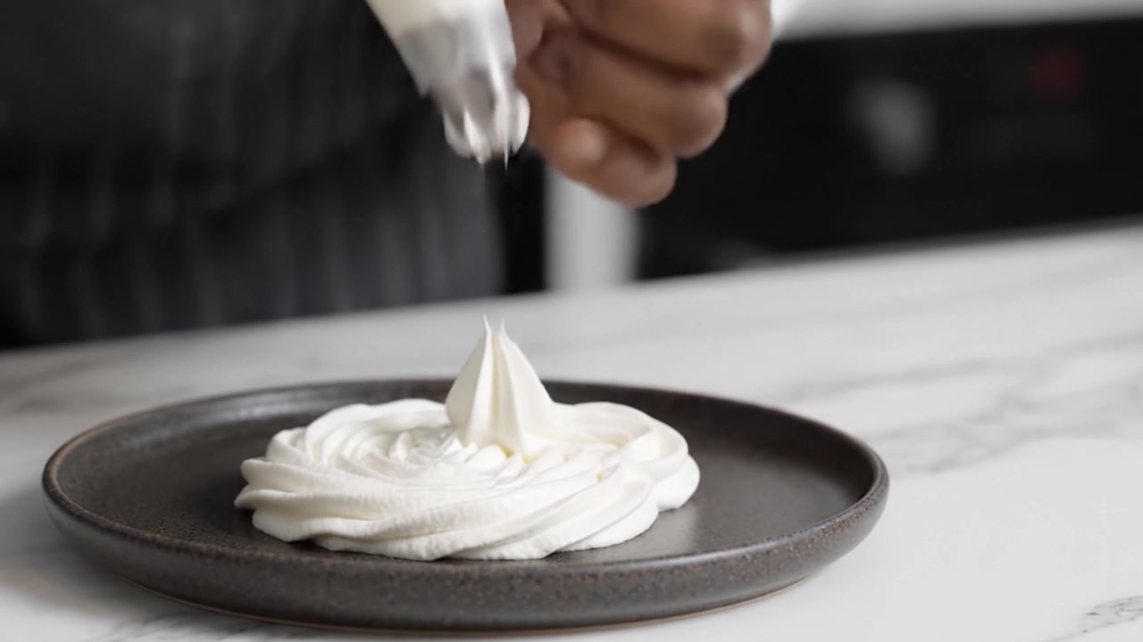 Um Artista Culinário Habilidosamente Decorando um Prato Simples com Chantilly, Demonstrando a Precisão e a Técnica da Decoração de Sobremesas em um Ambiente de Cozinha Profissional