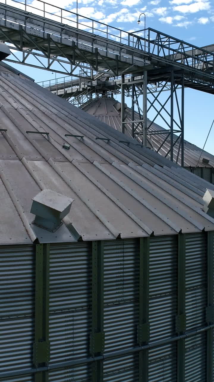 Large silver granary. Modern grain elevators. Metal industrial silos for agribusiness. New plant for storing crop. Close-up. Drone view. Vertical video
