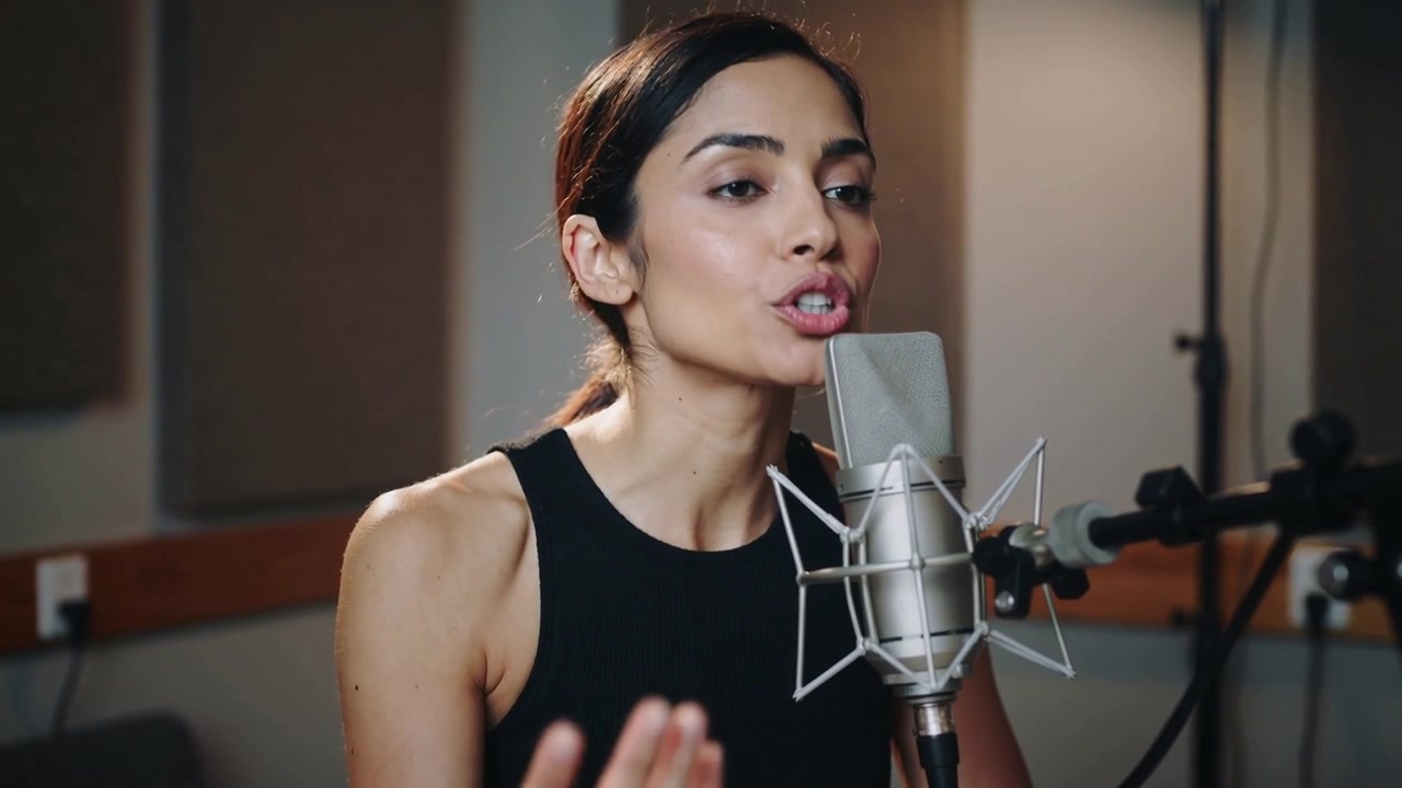 Una cantante respira e canta una frase in studio per la registrazione, indossando un top nero senza maniche e con un microfono.