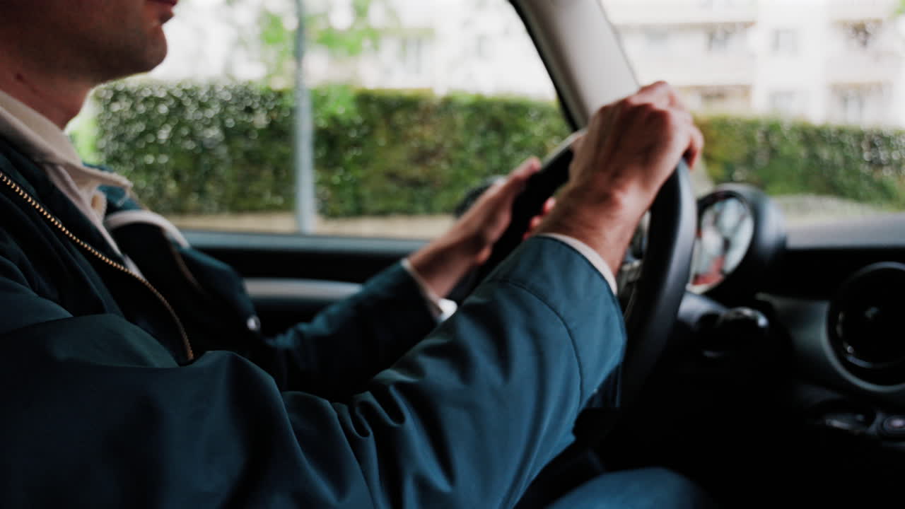 Close up of a man's hands on a steering wheel, driving a car on the road in the rain