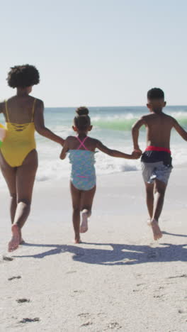 smiling african american family holding hands and running on sunny beach