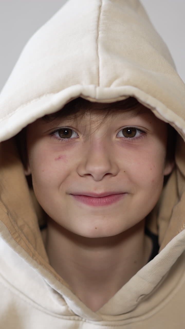 Smart good-looking teenage boy smiling to the camera. Dark-haired guy in a hood close up portrait. Vertical video