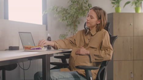 working pregnant woman eating nuggets during office lunch break