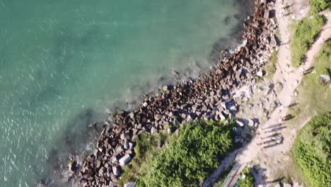 Aerial-footage-of-the-the-beautifu-rocks-and-sunny-beach-of-Armação-in-Florianópolis,-Brazil