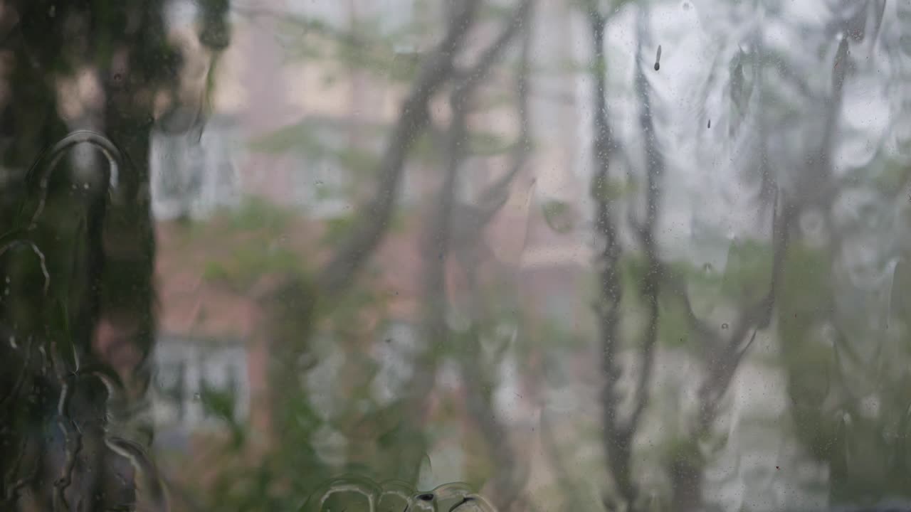 강한 물이 창문 유리창에 부히고 아래로 흘러내립니다. 근접 사진. 비가 오는 계절에 유리 바탕에 방울이 떨어집니다.