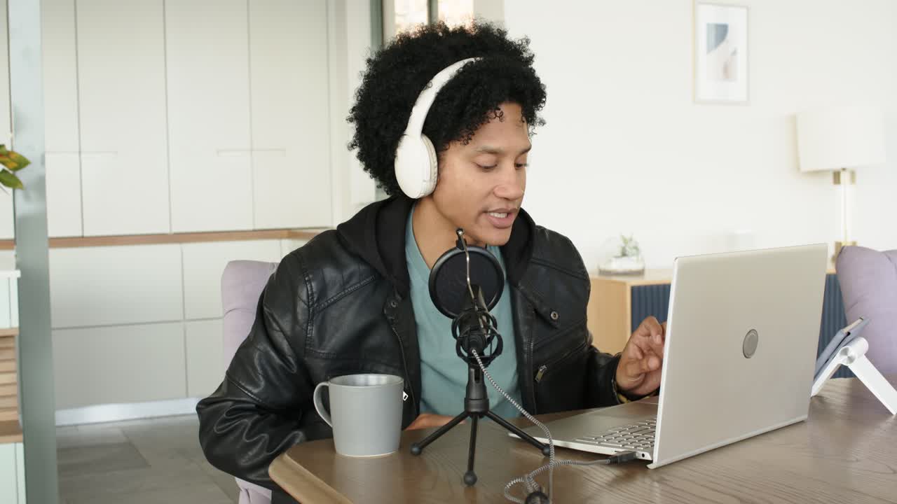 African American man at home aligning microphone for podcast typing on laptop checking smartwatch