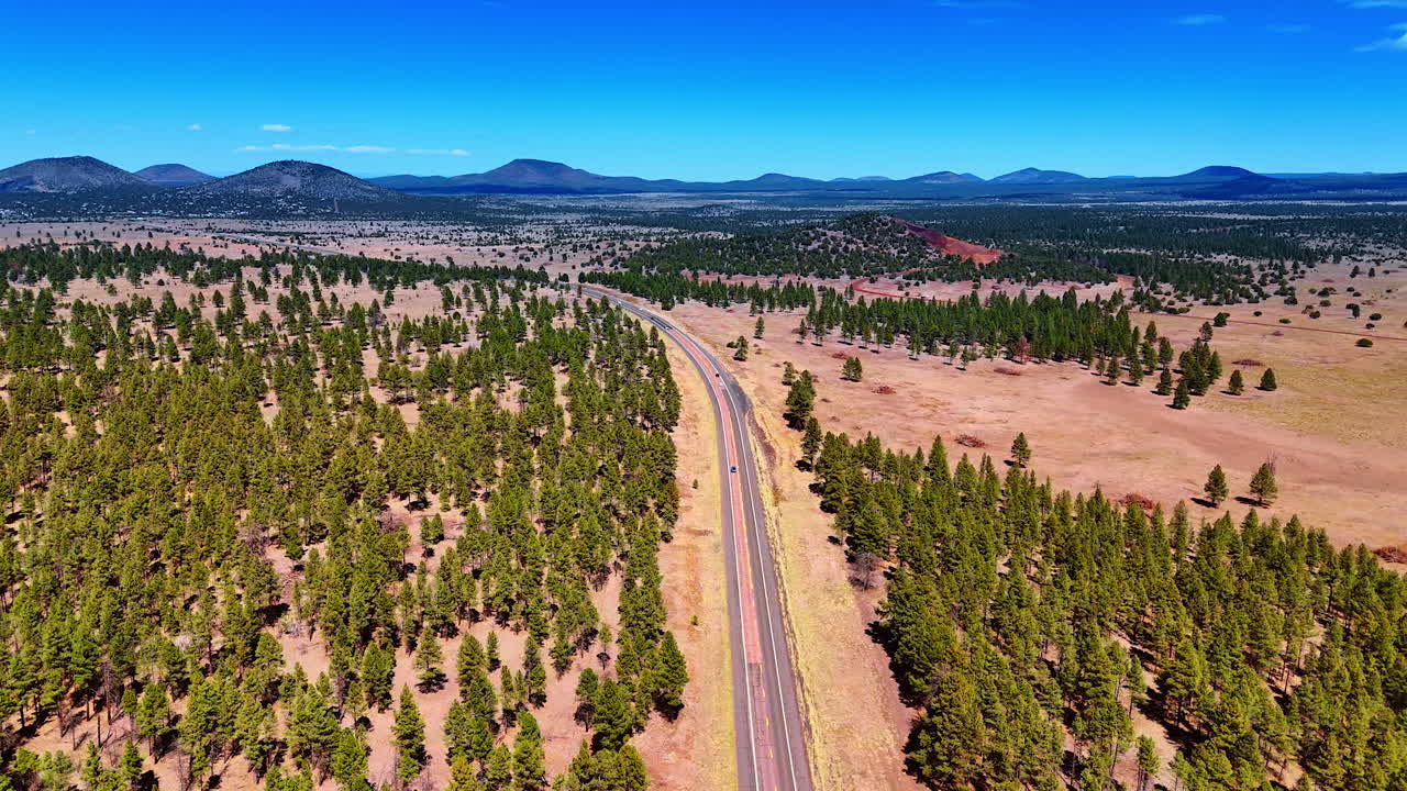 Footage above the highways in the valley covered with sparse pine tree forest. Mountain range at backdrop. Sceneries of Arizona State, USA