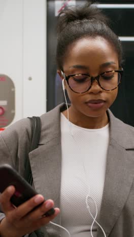 woman using phone and listening to music on a subway train