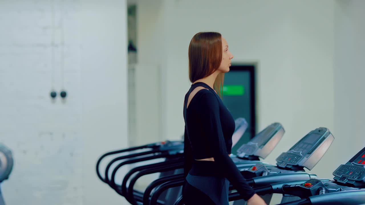 Young woman athlete is walking on a treadmill, warming up on a simulator in a sports hall. Treadmills stand in a row. Circular motion of the camera.