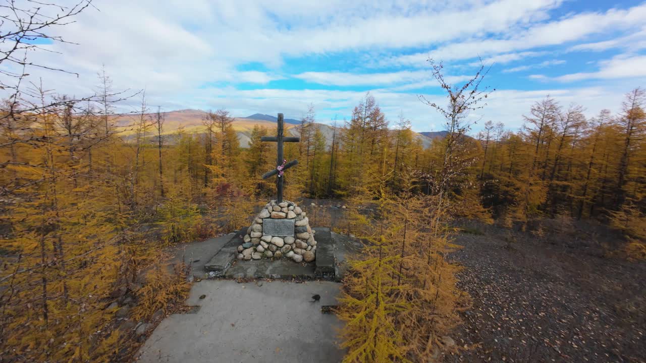 Experience the tranquility of Siberia's autumn, where golden larches create a stunning backdrop for a solitary cross. Nature's beauty shines in this peaceful wilderness.