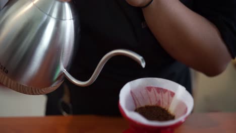 young male barista in trendy modern cafe coffee shop pours boiling water over coffee grounds making a pour over drip coffee