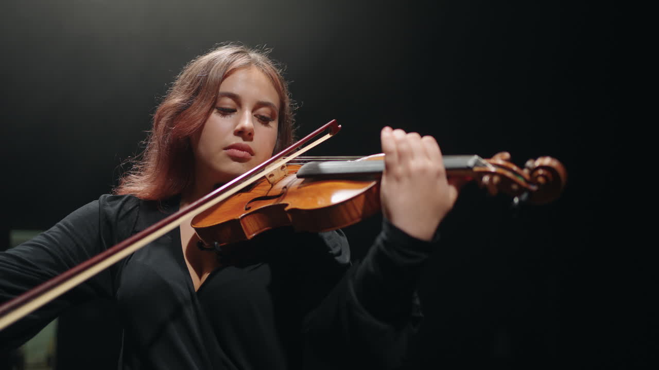 una violinista inspirada está tocando el violín en la escuela de música o un músico de sala de música oscura está tocando clásico