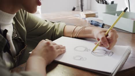 trabajadora biracial ocupada dibujando el diseño de un anillo en un estudio de joyas en cámara lenta