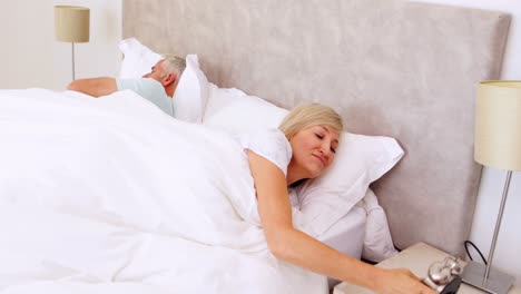 peaceful couple sleeping in bed with woman turning off alarm