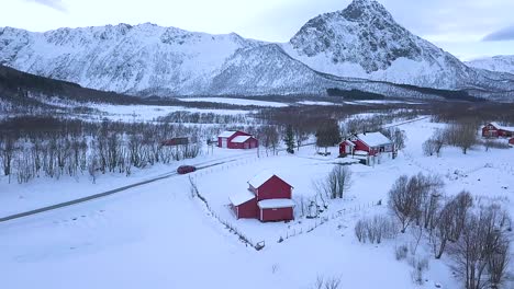 Coche-Que-Viaja-Por-Carretera-Rural-Cerca-De-Un-Pueblo-Tranquilo-Con-Cadenas-Montañosas-En-El-Fondo-Durante-El-Invierno-En-La-Isla-De-Andoya,-Noruega