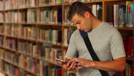 Concentrating-student-using-his-tablet-standing-in-the-library-