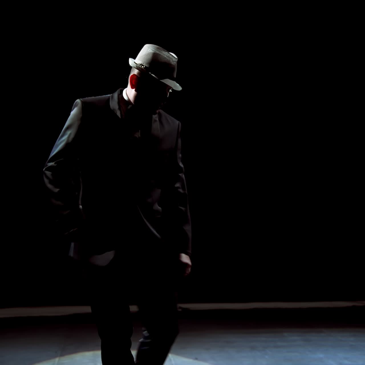 Actor making a performance on theater stage. Man in black suit putting on his hat and began dancing in darkness against spotlight