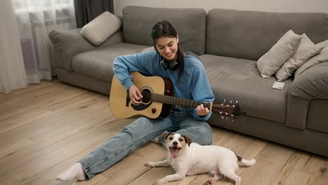 Una-Joven-Toca-La-Guitarra,-Sentada-En-El-Suelo-Con-Su-Adorable-Perro.