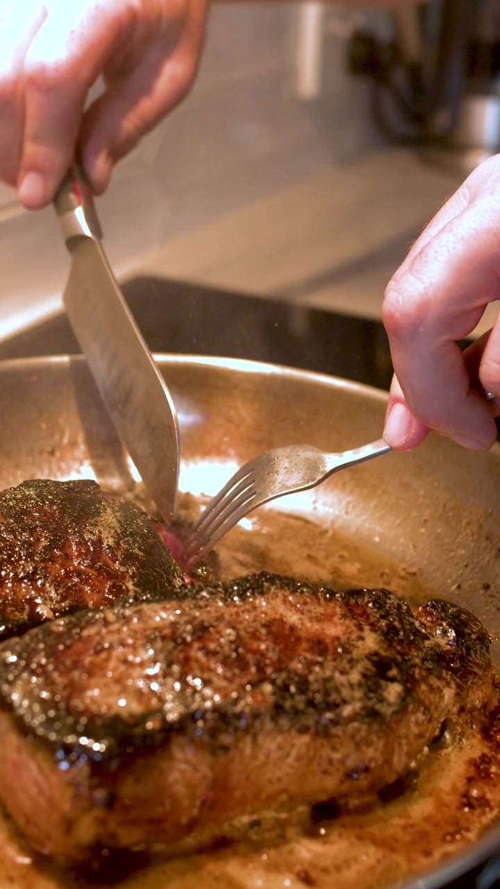 Primo piano di mani che usano coltello e forchetta per tagliare la carne di manzo in una padella