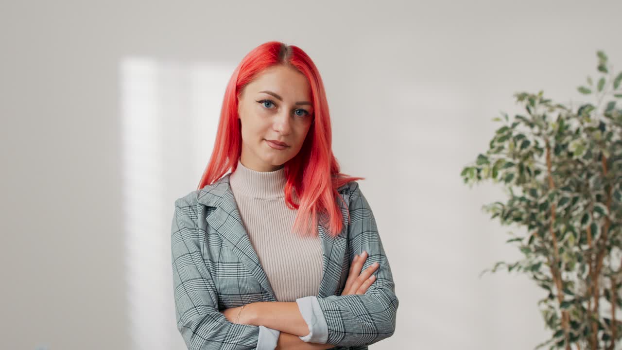 화려한 분홍색 머리카락의 여성은 빈 방에서  벽에 서 있습니다. 소녀는 가 위에 팔을 고 있습니다. 그녀는 카메라에 미소 짓고 있습니다. 부동산 에이전트, 보험 조정자, 기업 사무실 직원, 사업가.