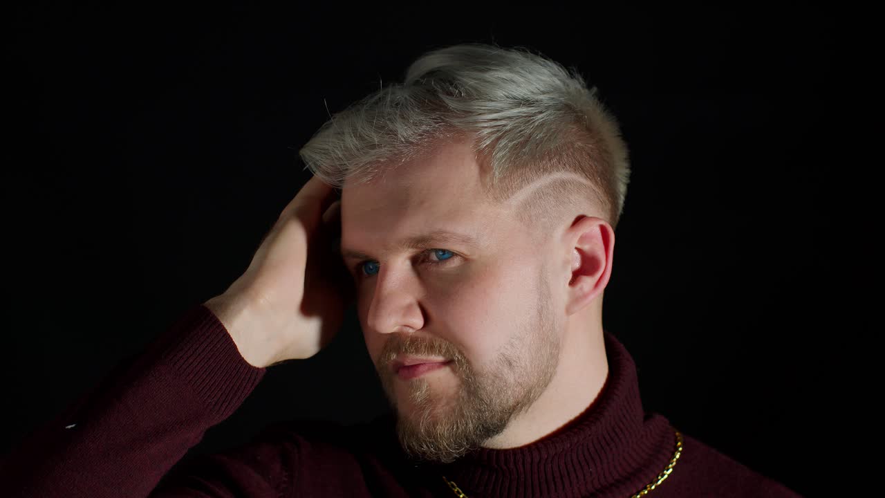 sonriente joven alegre en ropa elegante de moda sosteniendo la mano sobre la cabeza, mirando a la cámara