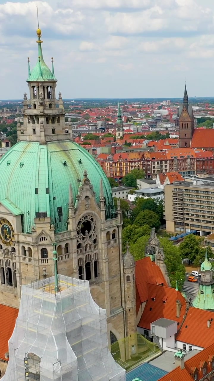 A cinematic vertical aerial drone shot of the iconic New City Hall Neues Rathaus in Hanover, Germany, featuring its green dome and historic architecture under a bright sky.