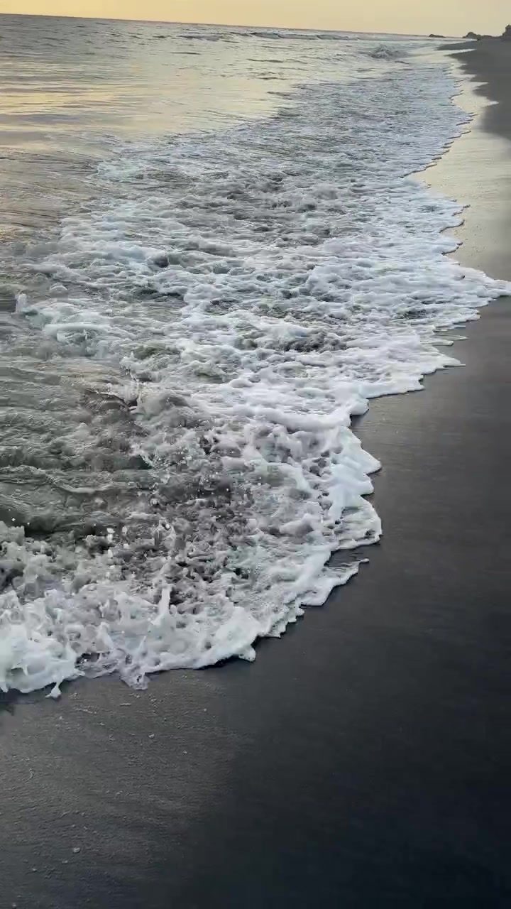 Dolci onde dell'oceano che si infrangono su una spiaggia di sabbia scura al tramonto