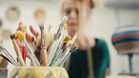 mujer creativa decorando una olla hecha a mano en el estudio, eligiendo pincel y pintura, cámara lenta