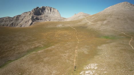 Toma-Aérea-De-Cuatro-Personas-Caminando-Por-Un-Sendero-Hacia-La-Montaña-Olympus-En-Un-Día-Soleado-De-Verano