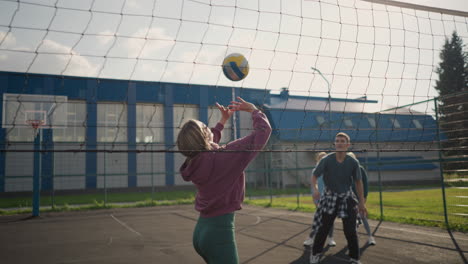 instructor training volleyball beginner with two women watching attentively in background, outdoor volleyball court with building visible in backdrop