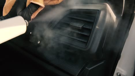 male wearing black gloves cleaning a dashboard side air vent with steam