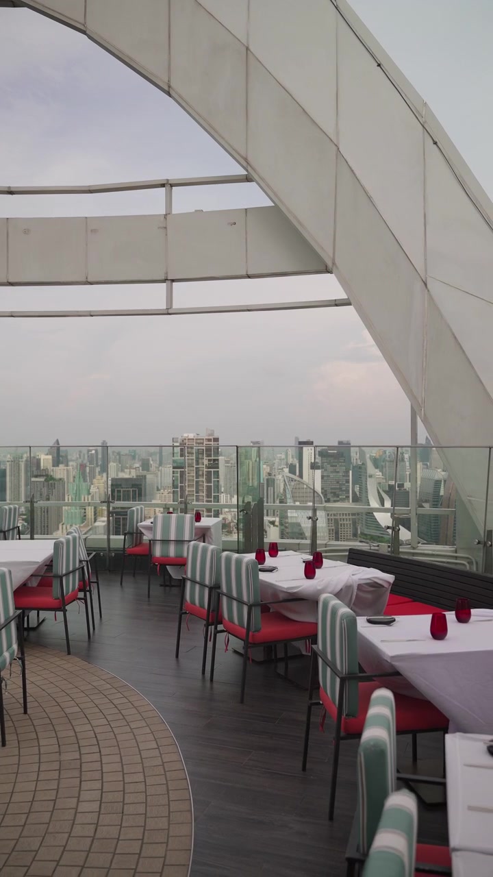 Mesas vacías de alta cocina puestas con cristalería roja en un restaurante en la azotea con vistas al horizonte de Bangkok, Tailandia. 4K Vertical