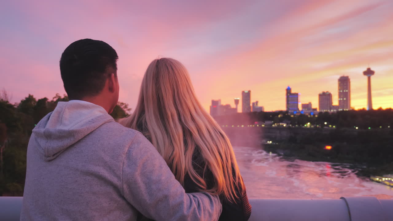 미국과 캐나다 사이의 다리에 서서 아름다운 일몰을 감상하는 다민족 커플