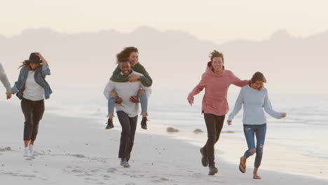 group of friends having fun running along winter beach together