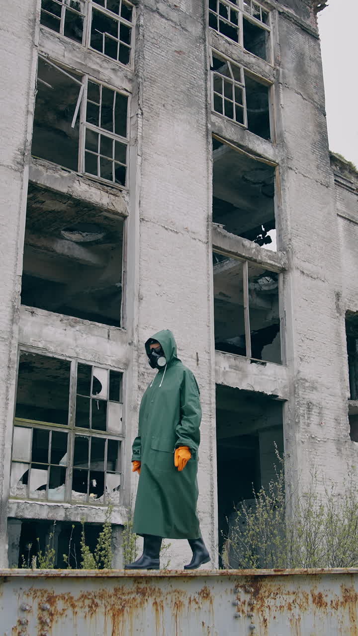 Person in radioactive zone. Human in chemical protective suit and mask walking on the background of destroyed buildings. Biological attack. Vertical video