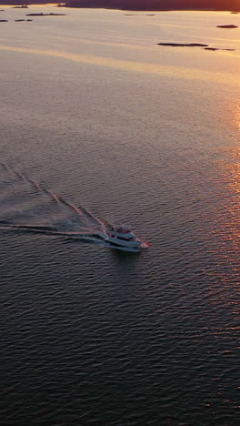 vertical drone shot around a boat driving in calm, reflecting sea, summer sunset