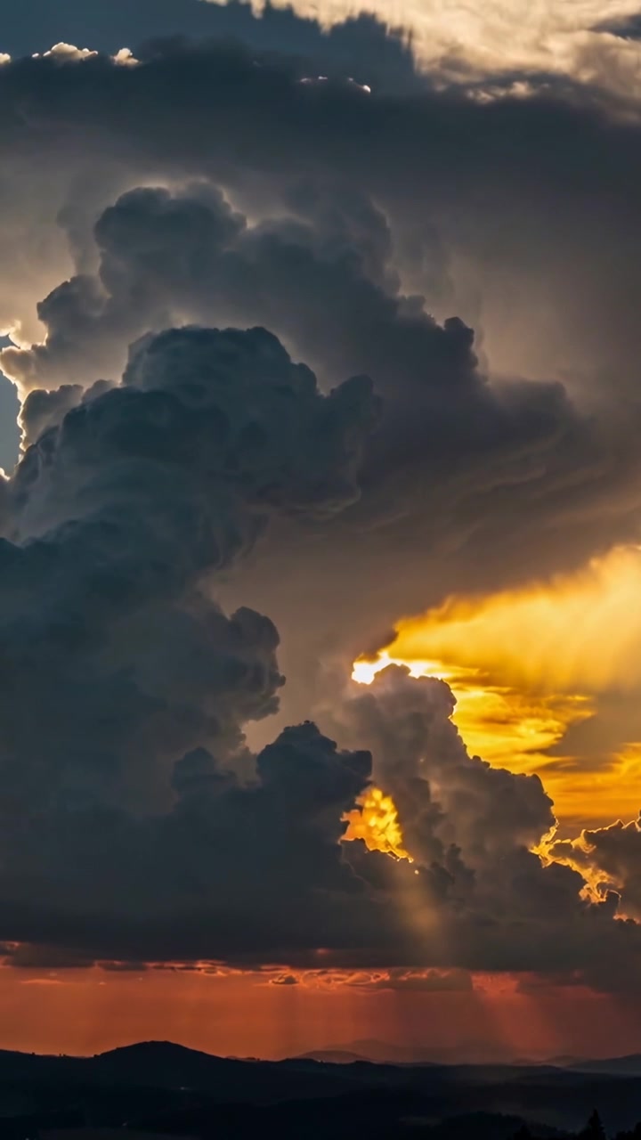 Vertical video: Glowing cumulonimbus reacting to sun breaking through gap, casting rays to hills